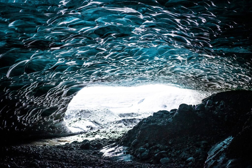 Interior of a glacial ice cave beneath Vatnajökull glacier, Iceland — blue glacial ice ceiling lit from the cave entrance in winter
