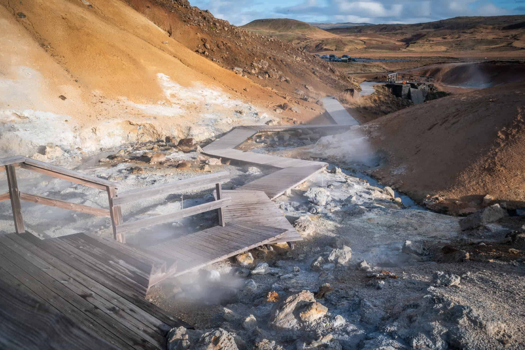 Wooden boardwalk through geothermal area in Iceland, steam rising from hot springs — marked paths protect fragile volcanic ground