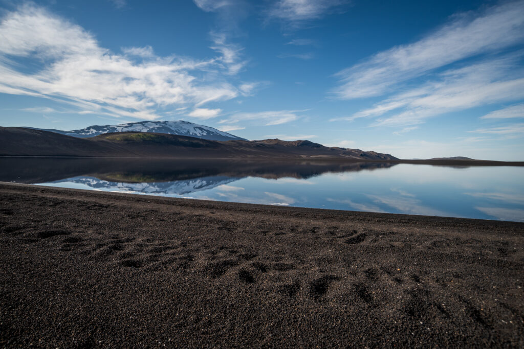 Volcanic lake with perfect reflection of a snow-capped mountain on the Landmannalaugar plateau, Iceland — black sand shore in the foreground, accessible only via F-road