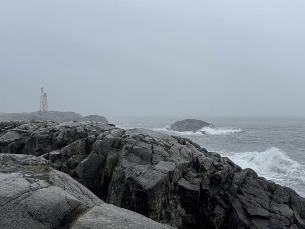 Stokksnes lighthouse in fog with rough Atlantic waves breaking on dark volcanic rock, Stokksnes peninsula, southeast Iceland
