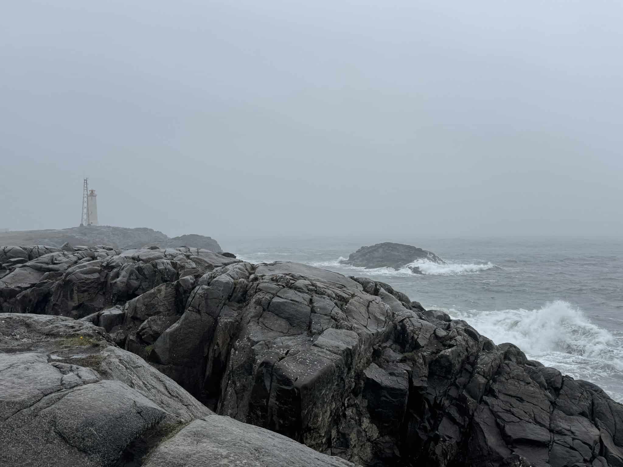 Stokksnes lighthouse in fog with rough Atlantic waves breaking on dark volcanic rock, Stokksnes peninsula, southeast Iceland