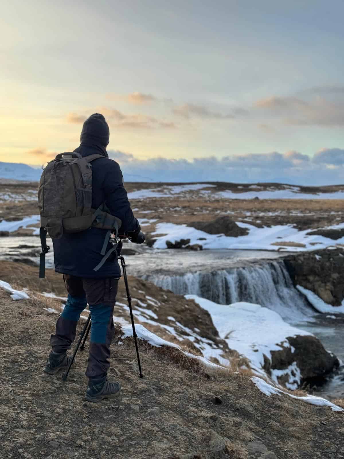 Marcel Strobel photographing a frozen waterfall in Iceland in winter conditions — with tripod and camera backpack