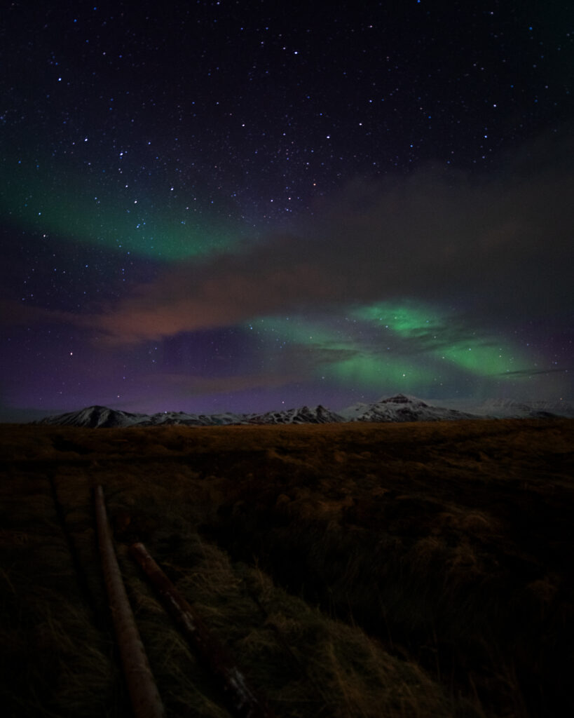 Faint northern lights over snow-capped mountains in Iceland at night — a low KP display captured with a wide-angle lens and long exposure, showing more than the naked eye sees
