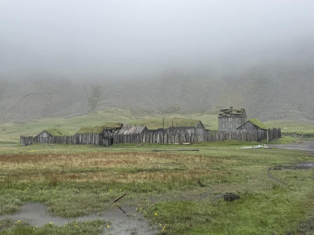 Viking Village film set at Stokksnes, Iceland — weathered wooden structures and turf roofs in fog at the foot of Vestrahorn mountain
