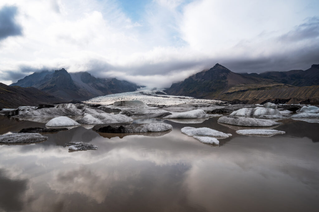 Kvíárjökull glacier lagoon, south Iceland — floating ice fragments in the foreground with the glacier tongue and surrounding mountains reflected in the still water surface