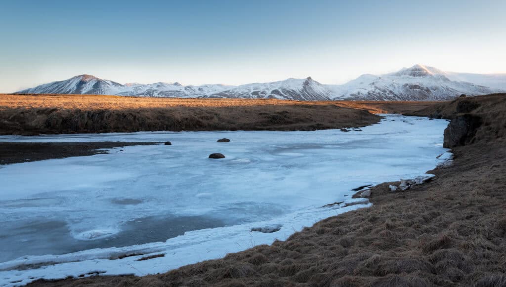 Frozen river and snow-capped mountain range in winter light, Iceland — photographed by Marcel Strobel